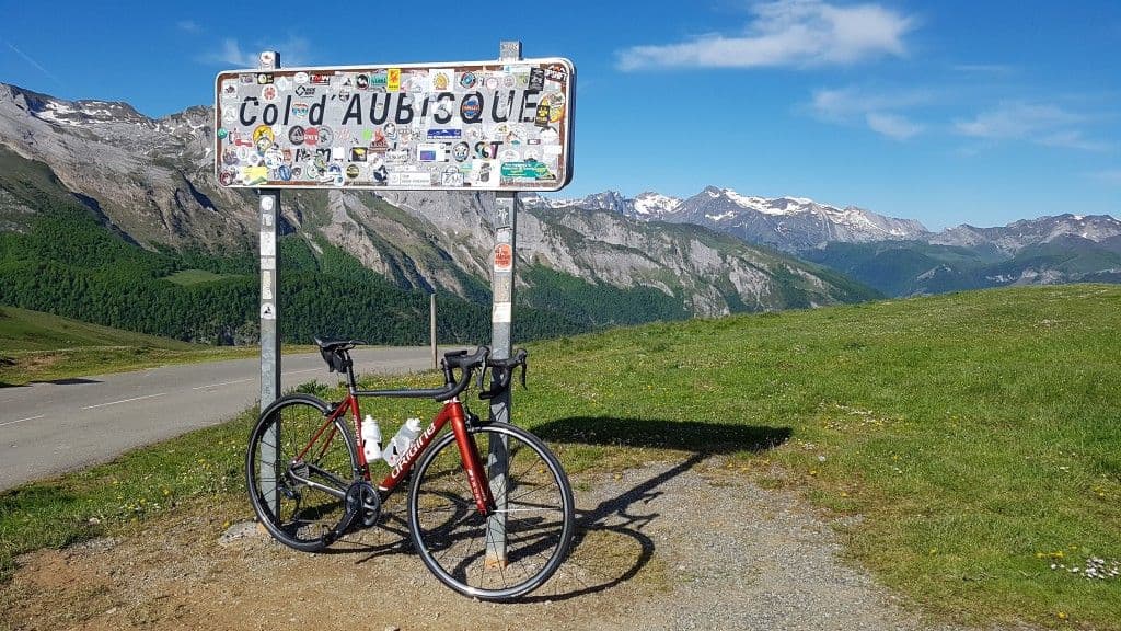 A bicycle resting against the Col d'Aubisque summit sign, surrounded by breathtaking views of the Pyrenees mountains.