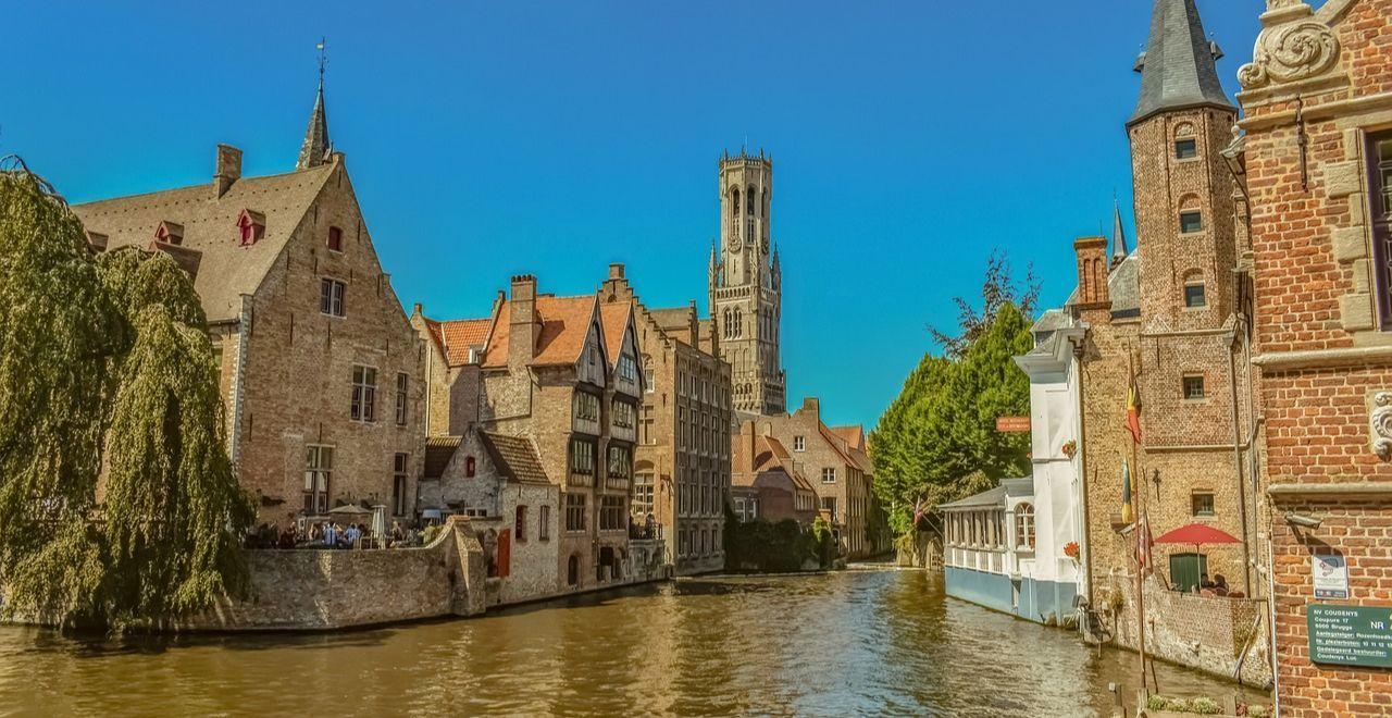 Picturesque view of Bruges canal with historic architecture and lush trees.