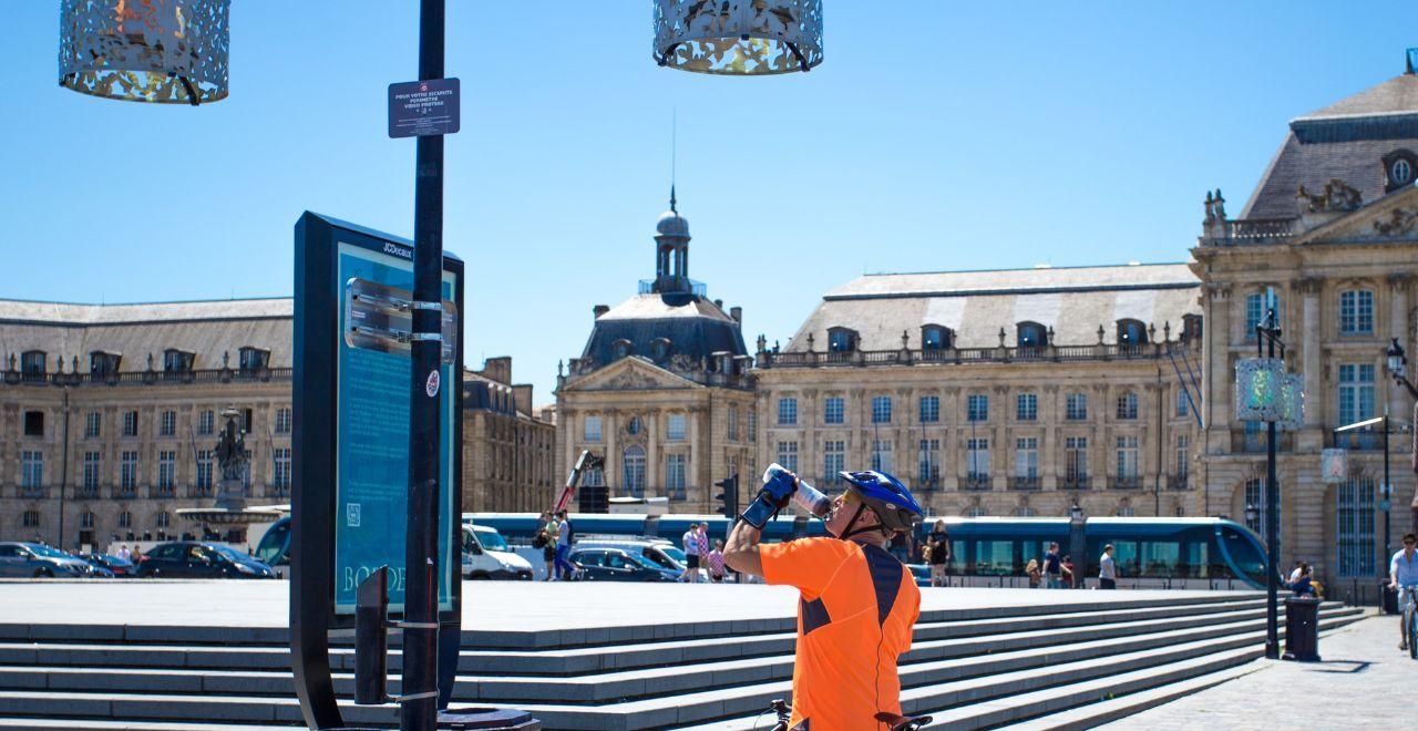 Cyclist in orange drinking water in front of Place de la Bourse, Bordeaux.