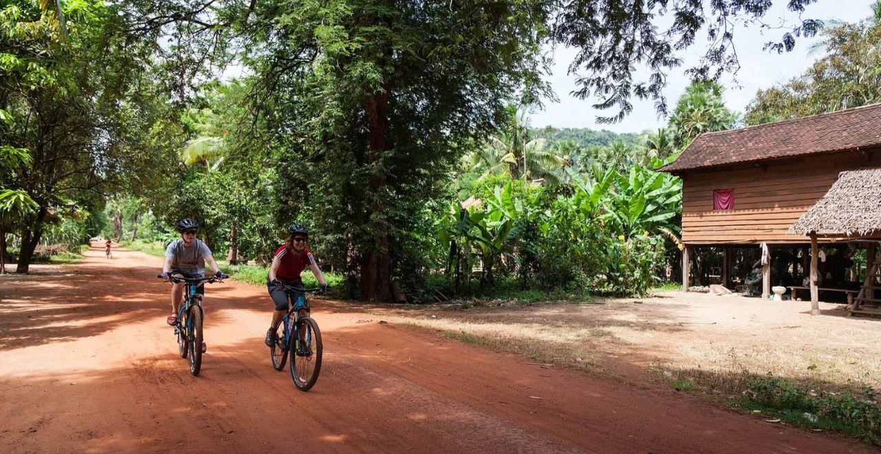 Two cyclists riding on a dirt road, tropical rural setting