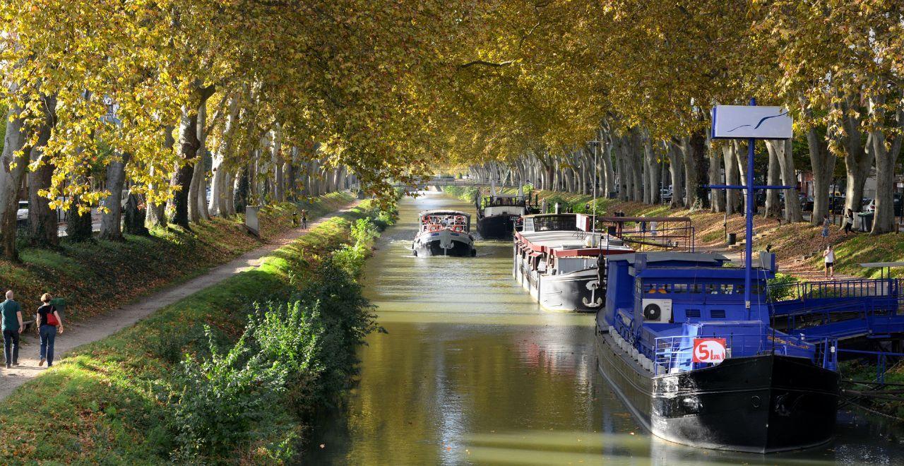 Boats on Canal du Midi lined with autumn trees.