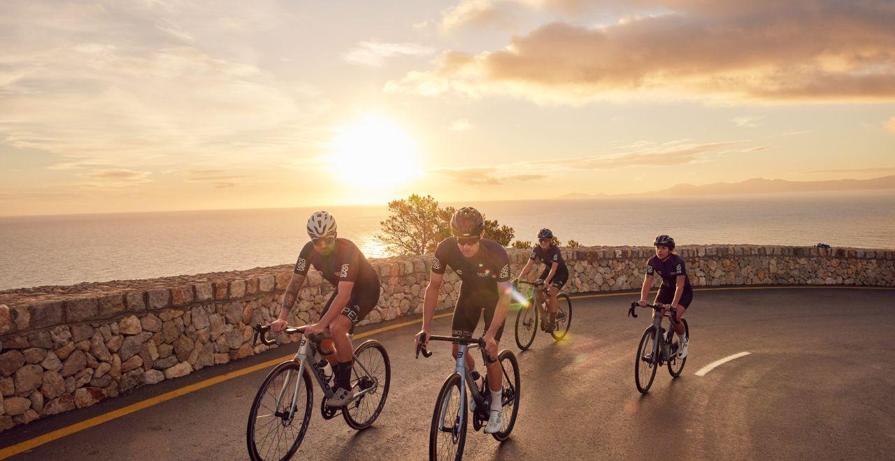 Group of cyclists riding by the ocean at sunrise