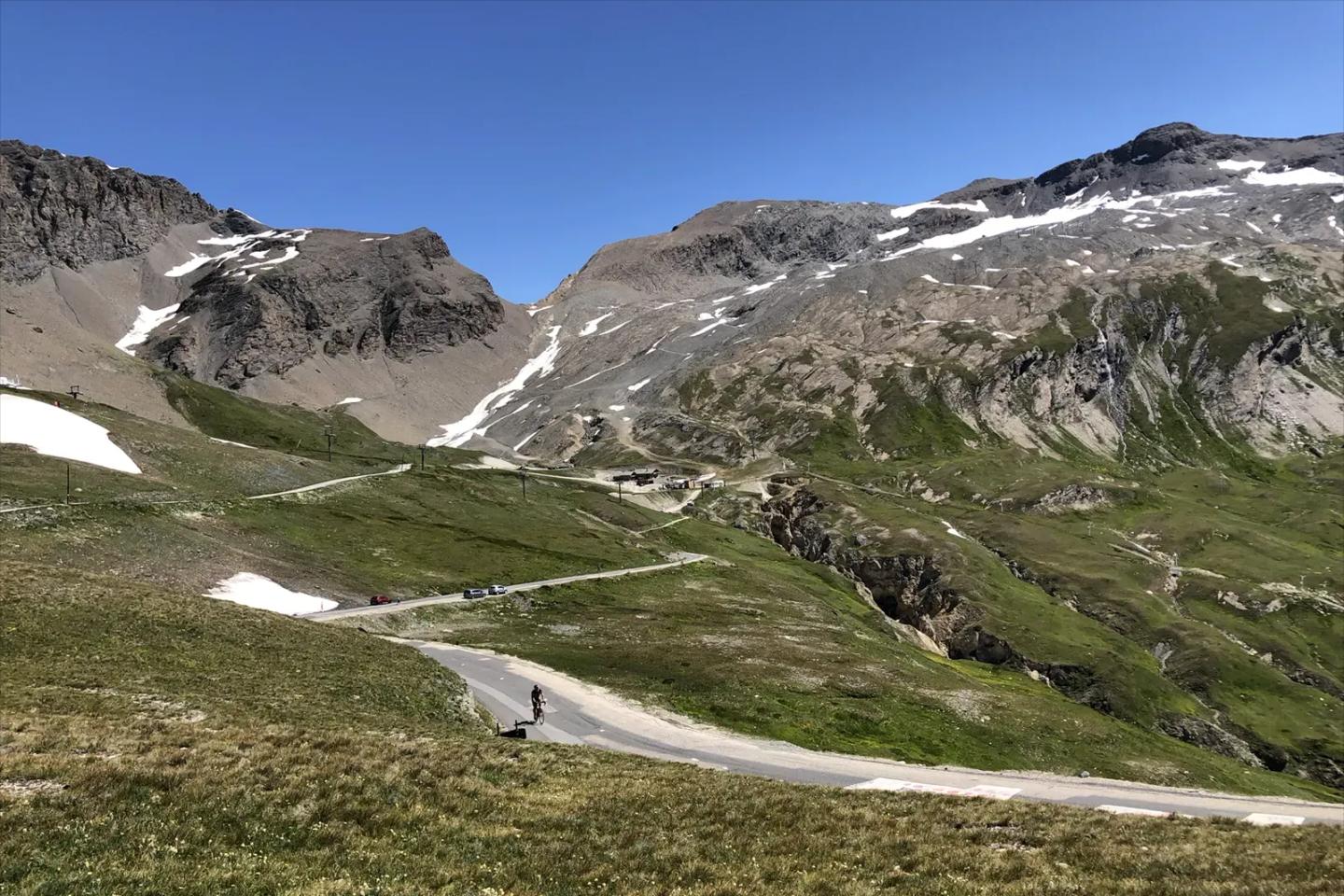 A winding road through the Col de l'Iseran with rugged mountains and patches of snow, under a clear blue sky.