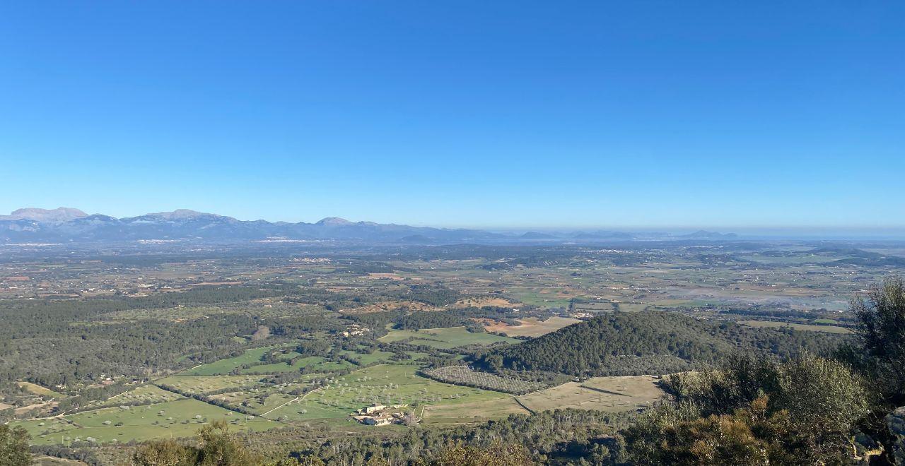 Panoramic view of a valley with fields, forests, and distant mountains.