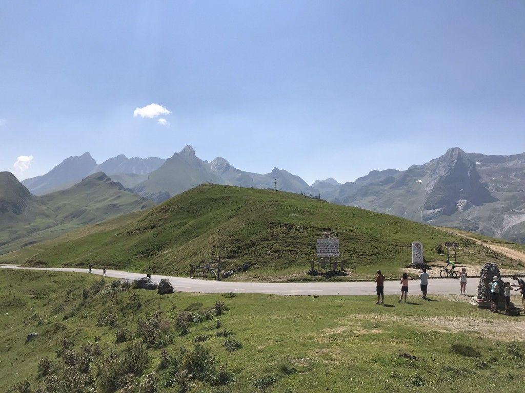 Scenic landscape of Col du Soulor with people at the top, mountains in the background.