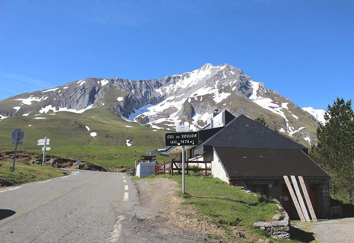 View of Col du Soulor sign at the summit, surrounded by snowy mountain peaks.