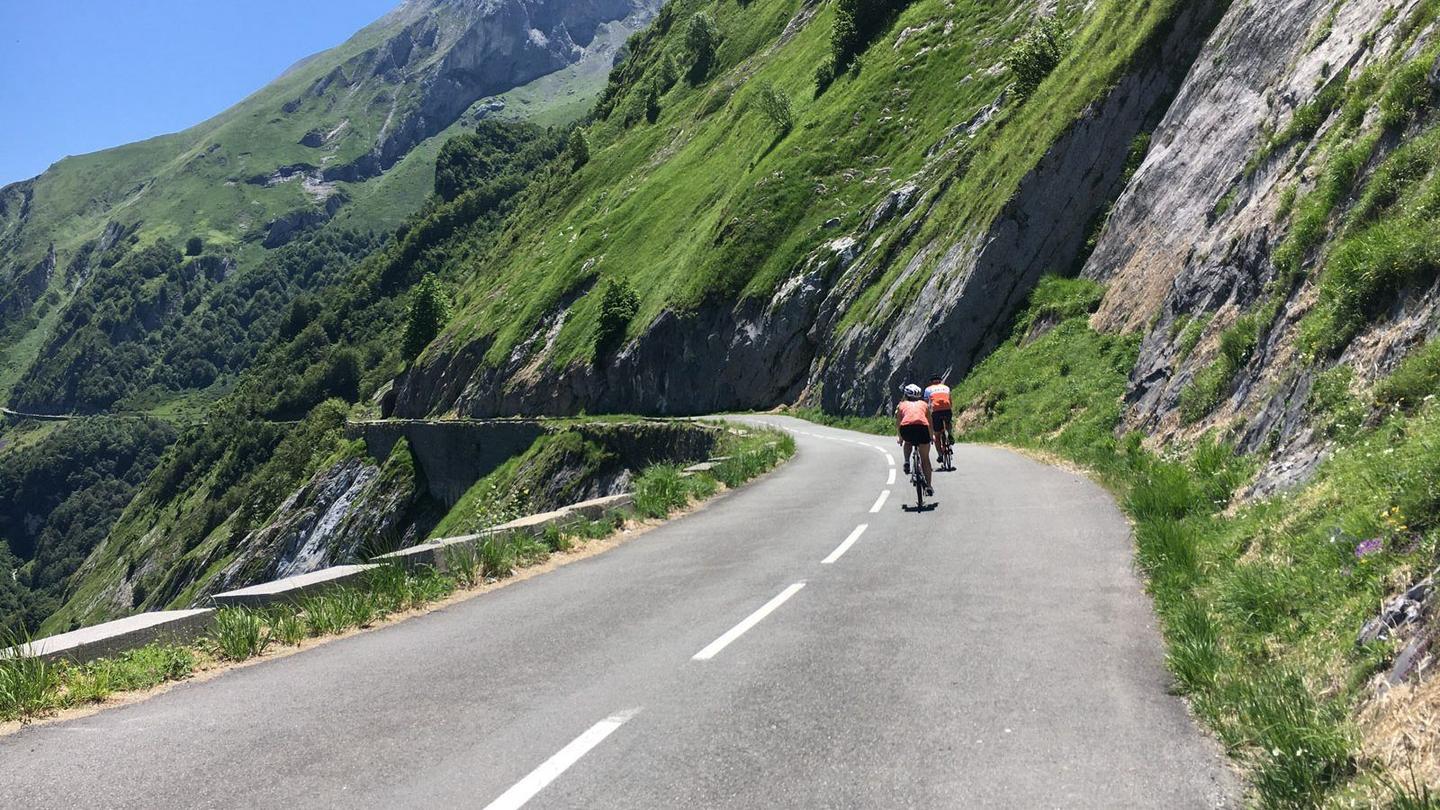 Cyclists ascending the Col du Soulor with lush green mountains and cliffs in the background.