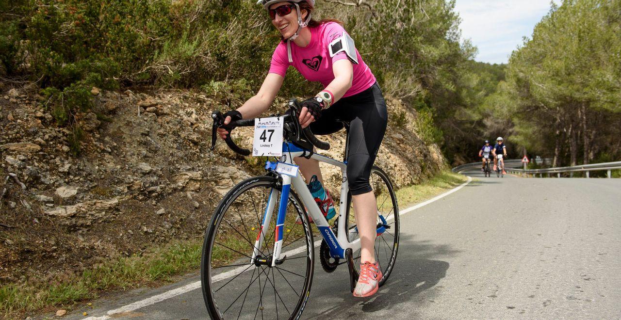 Female cyclist in a pink jersey smiling while riding uphill.