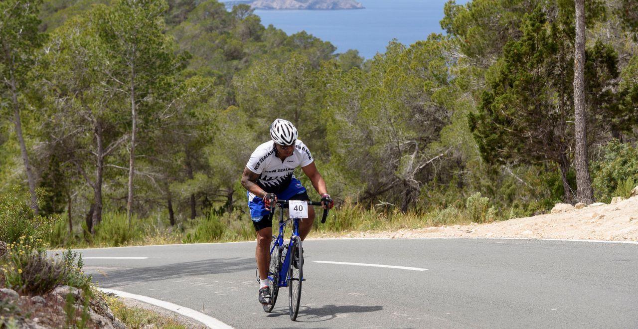 Cyclist in a white jersey riding uphill with ocean in the background.