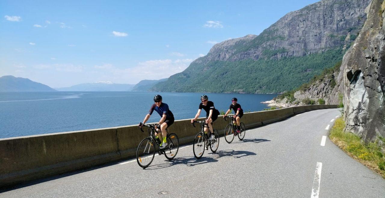 Three cyclists riding on a scenic mountain road by the lake.