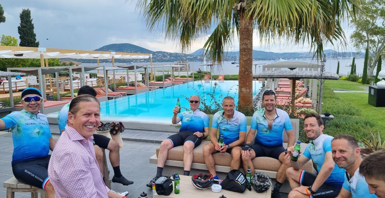 Cyclists in blue jerseys relaxing by a pool with drinks.