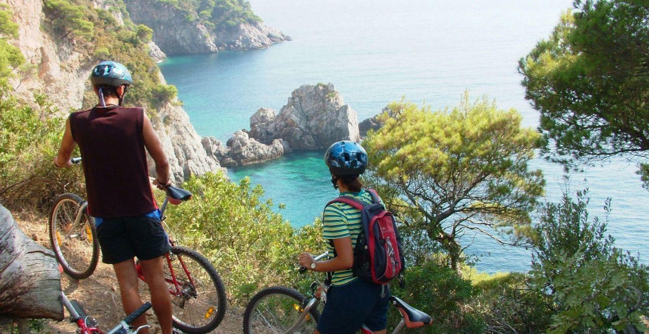 Cyclists enjoying a scenic overlook of a serene cove on a cycling route, surrounded by lush Mediterranean greenery.