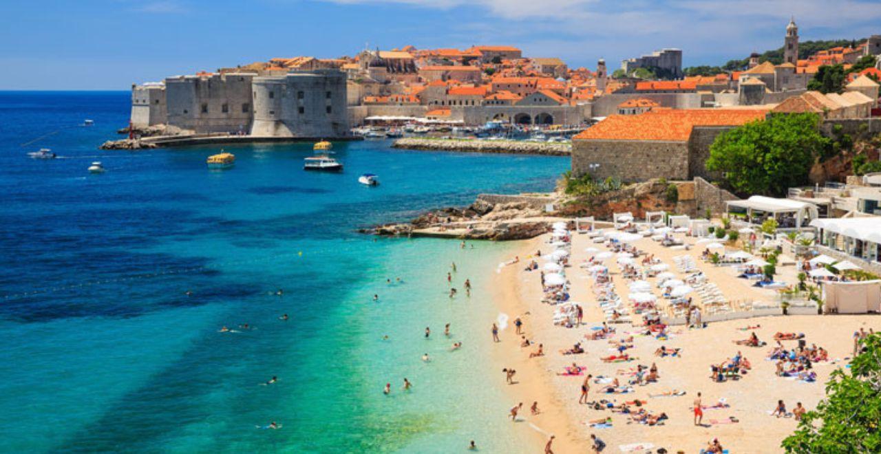 Panoramic view of Dubrovnik's old city and beach, showcasing the stunning architecture and vibrant tourist life by the Adriatic Sea