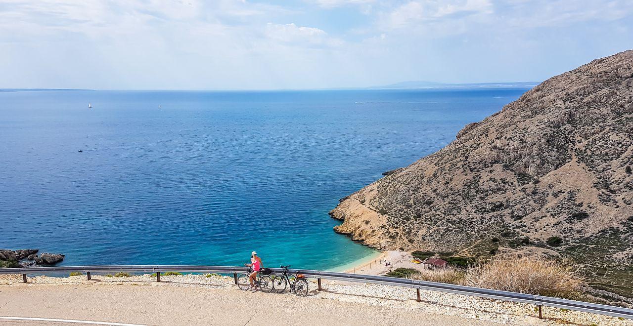 Cyclist pausing to enjoy the breathtaking view of a secluded beach framed by steep cliffs, celebrating the joys of coastal biking