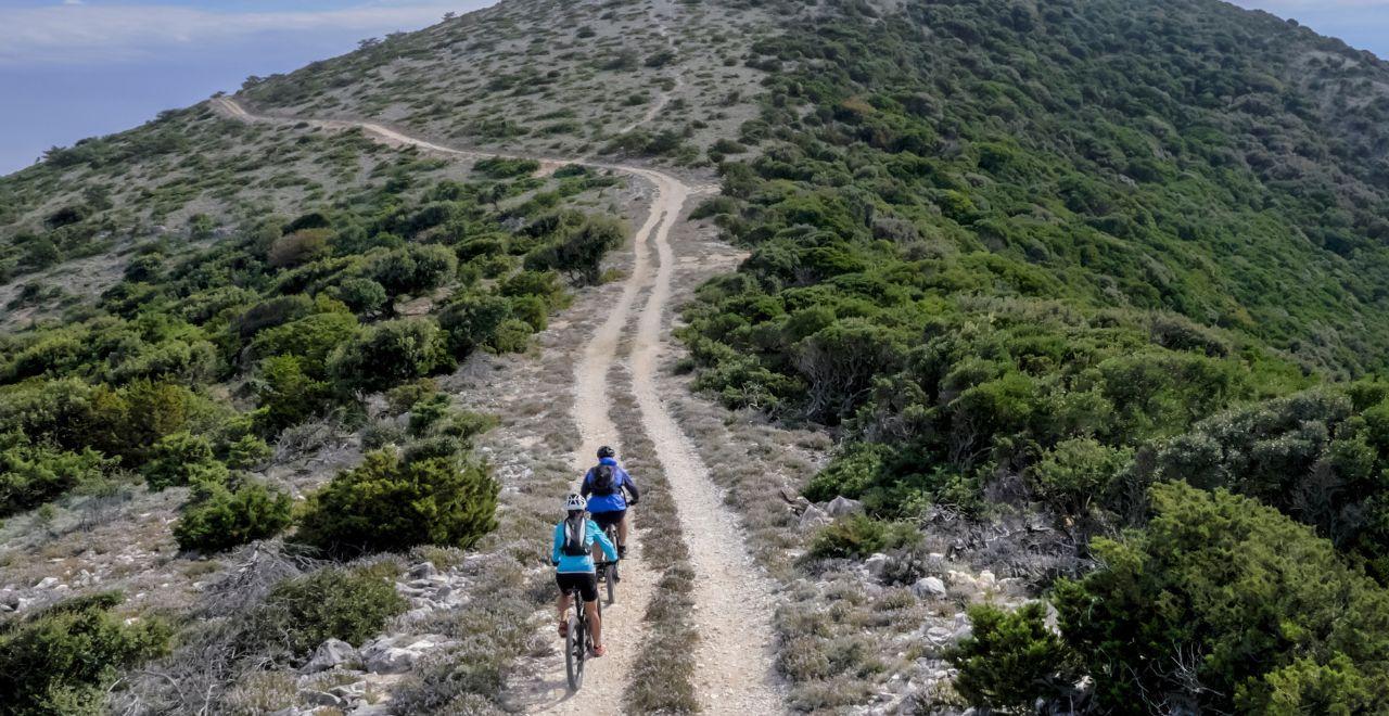 Mountain bikers tackling a steep off-road trail in a Mediterranean landscape, challenging themselves in the wild terrain