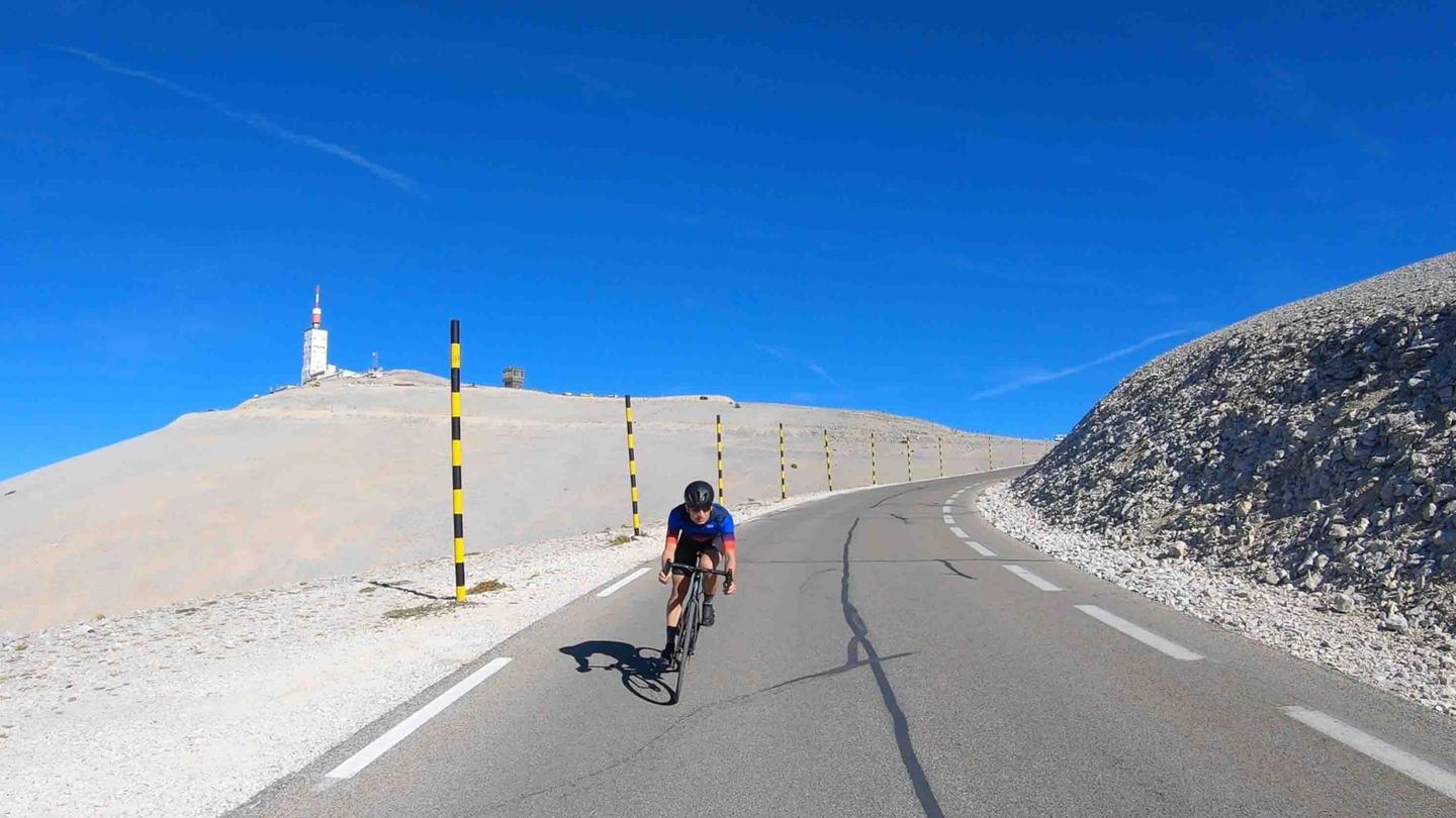 Cyclist climbing the scenic Mont Ventoux, surrounded by stark, rocky landscape under a clear blue sky.