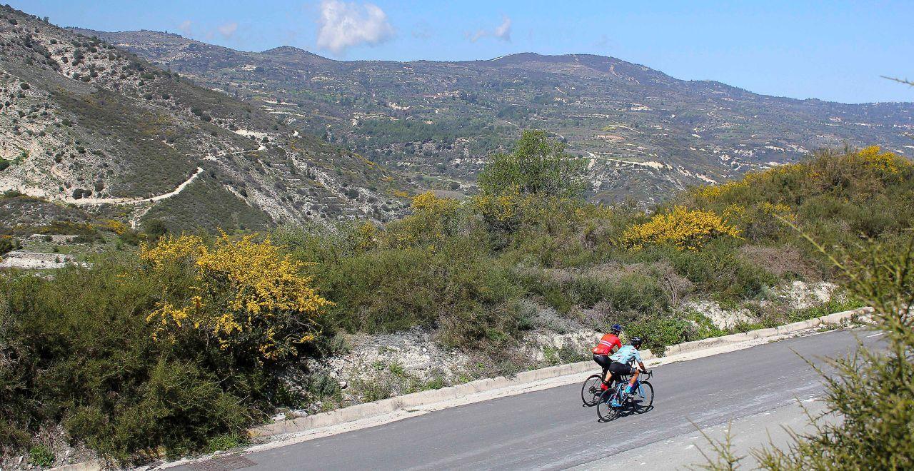 Cyclist pausing on a cliffside route in Cyprus, overlooking a secluded beach and crystal-clear waters, great for combining cycling with scenic stops