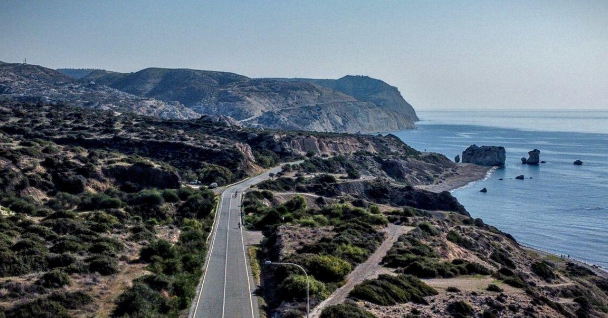 Serene coastal road meandering through a rugged landscape with sparse vegetation and a clear blue sky