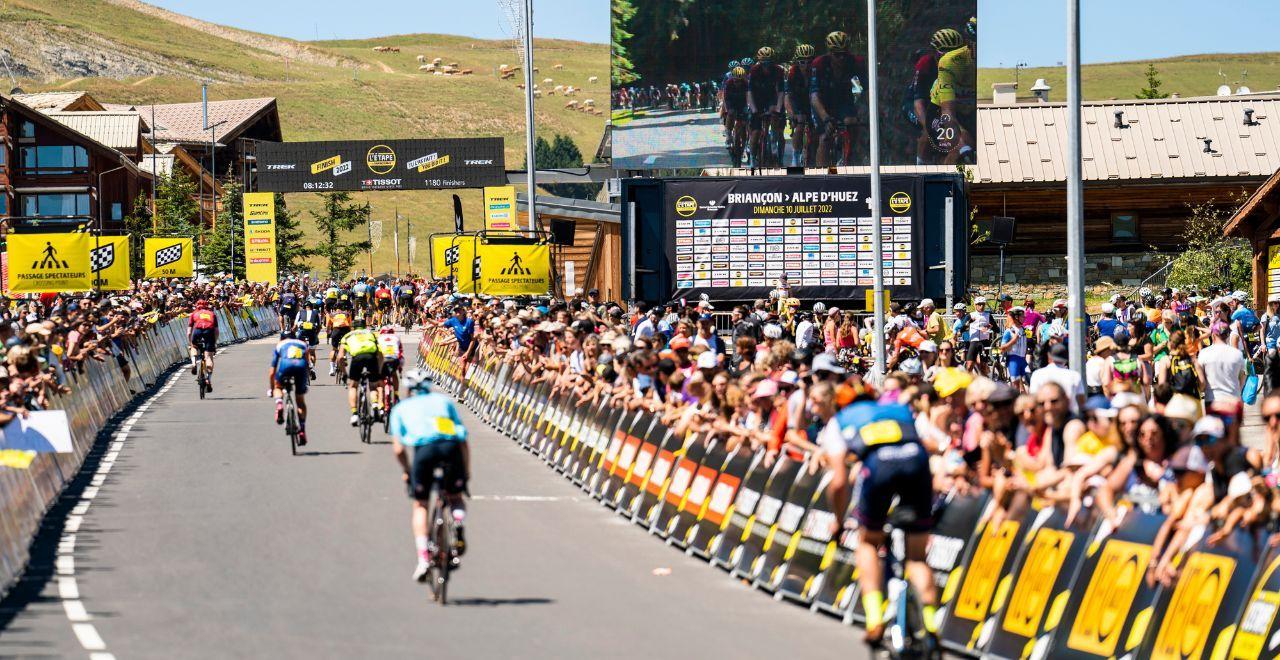 Cyclists approaching the finish line with spectators and a large screen.