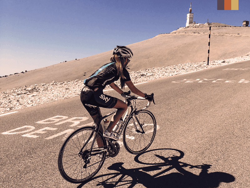 Female cyclist ascending Mont Ventoux, France, with a clear blue sky and the observatory in the background