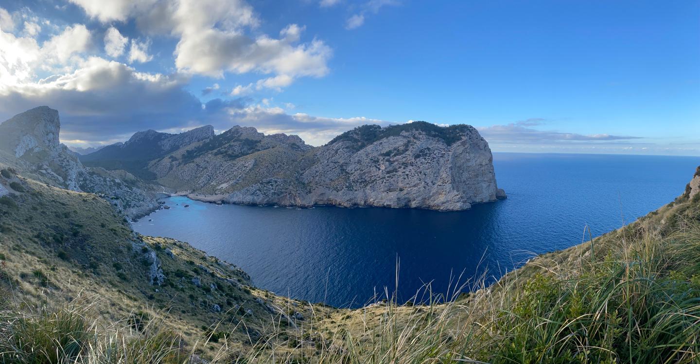 Stunning view of the coastline near Cap Formentor, with rocky cliffs and clear blue waters under a bright sky with scattered clouds.