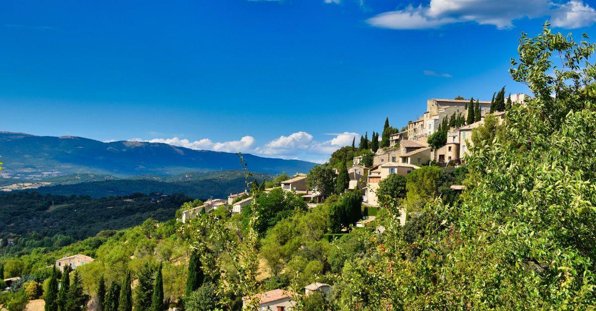 Hillside view of a quaint village in Provence, France, with lush greenery and mountain backdrop