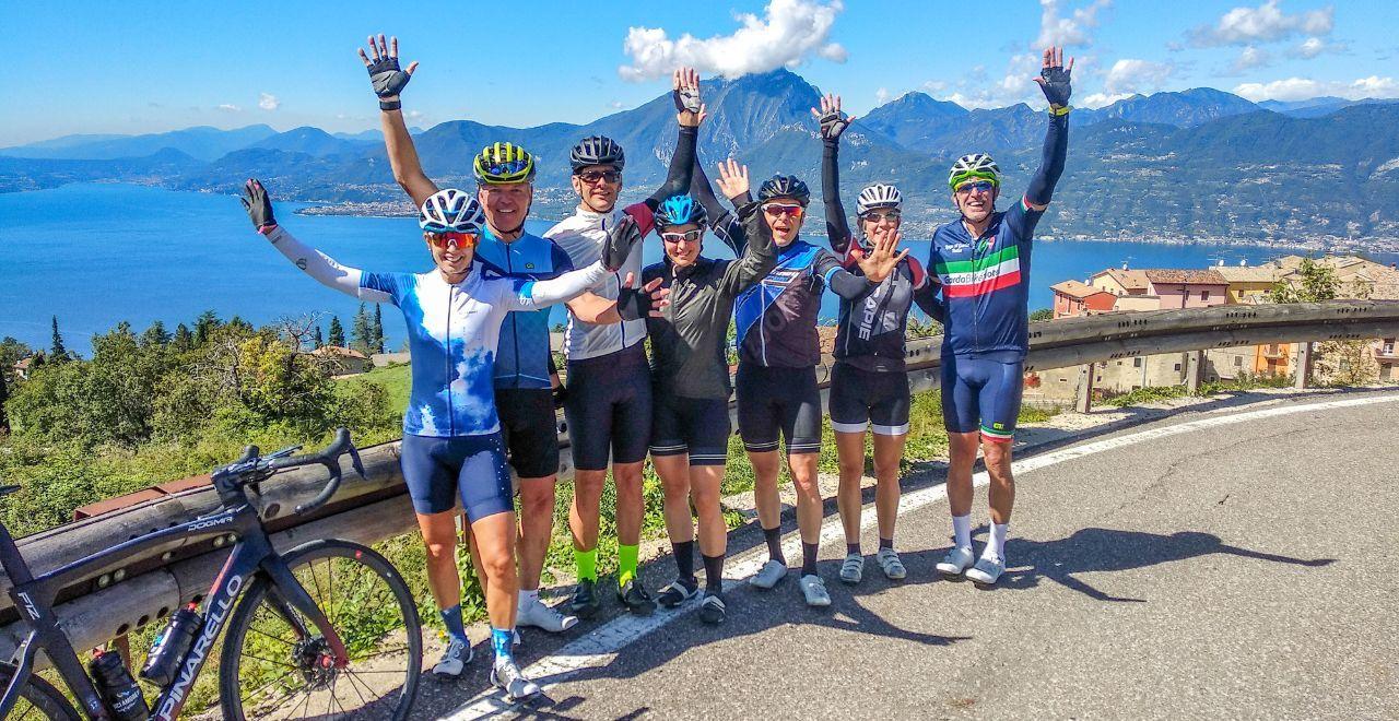 Group of cyclists posing with raised arms overlooking a scenic lake.