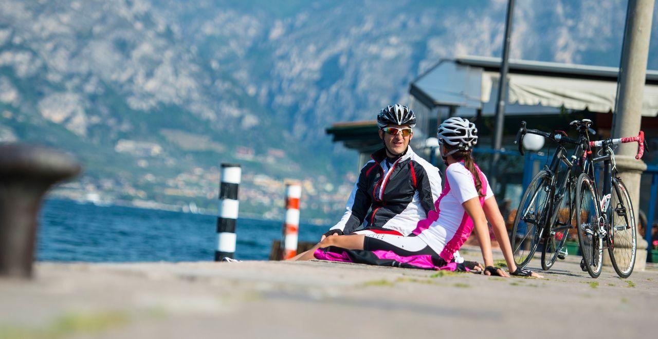 a male and female cyclist sitting on a dock with their feet in the water