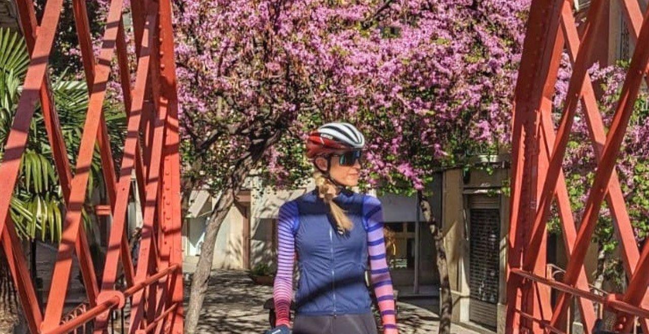 female cyclist standing on a bridge beneath pink blossom