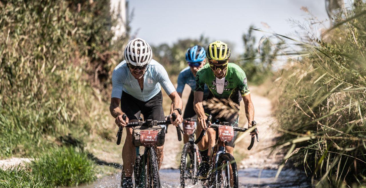 Cyclists racing through a wet trail with water splashing.