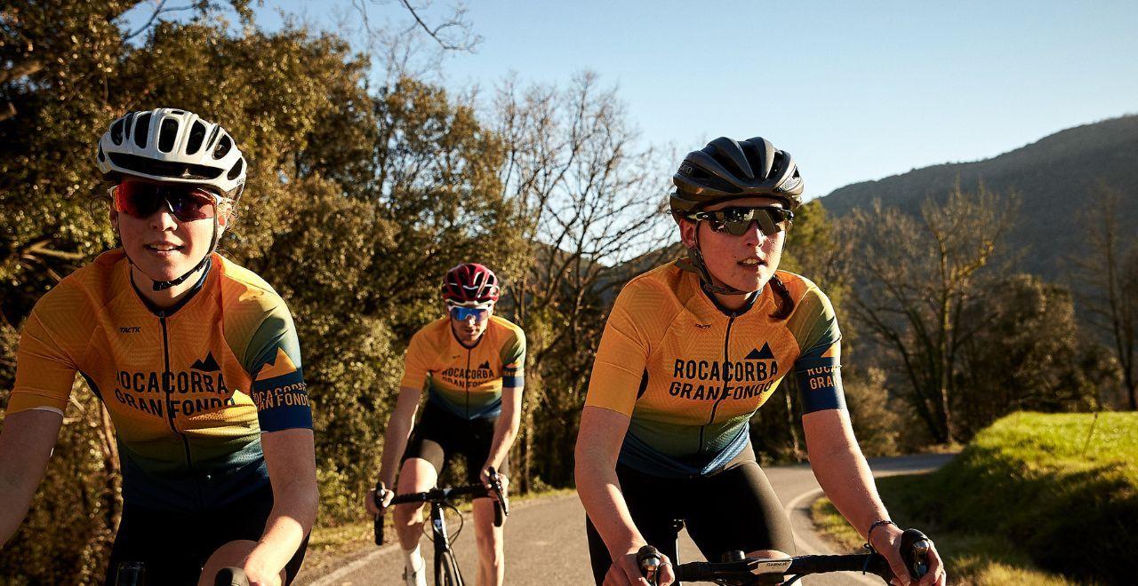 Three cyclists wearing matching jerseys riding on a scenic road.