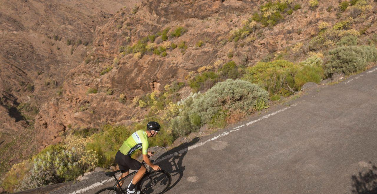 Cyclist riding uphill on a mountain road with rocky terrain.