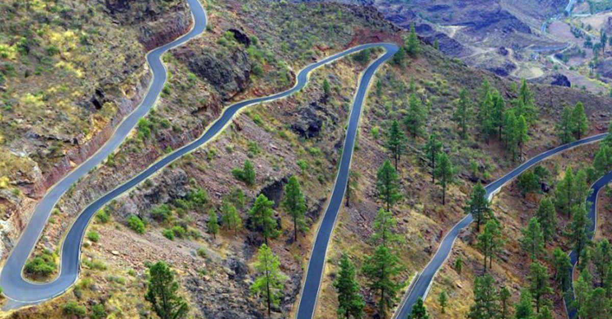 Aerial view of a serpentine road with multiple switchbacks winding through a rocky, forested landscape