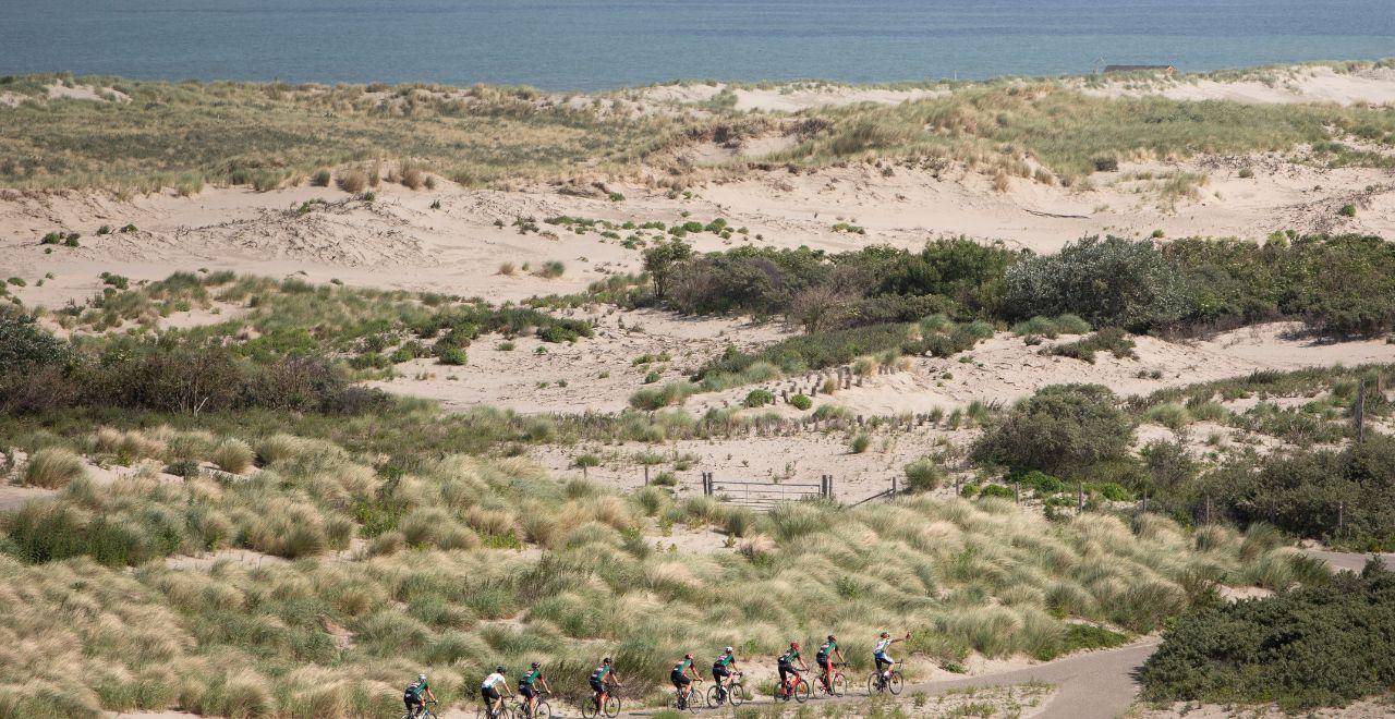Group of cyclists riding through sandy dunes and vegetation by the sea