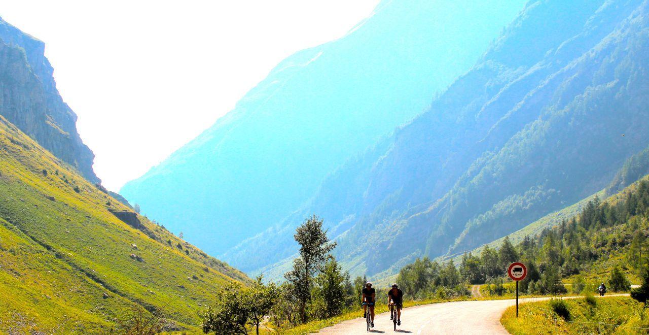 Two cyclists riding on a road between steep green mountain slopes.