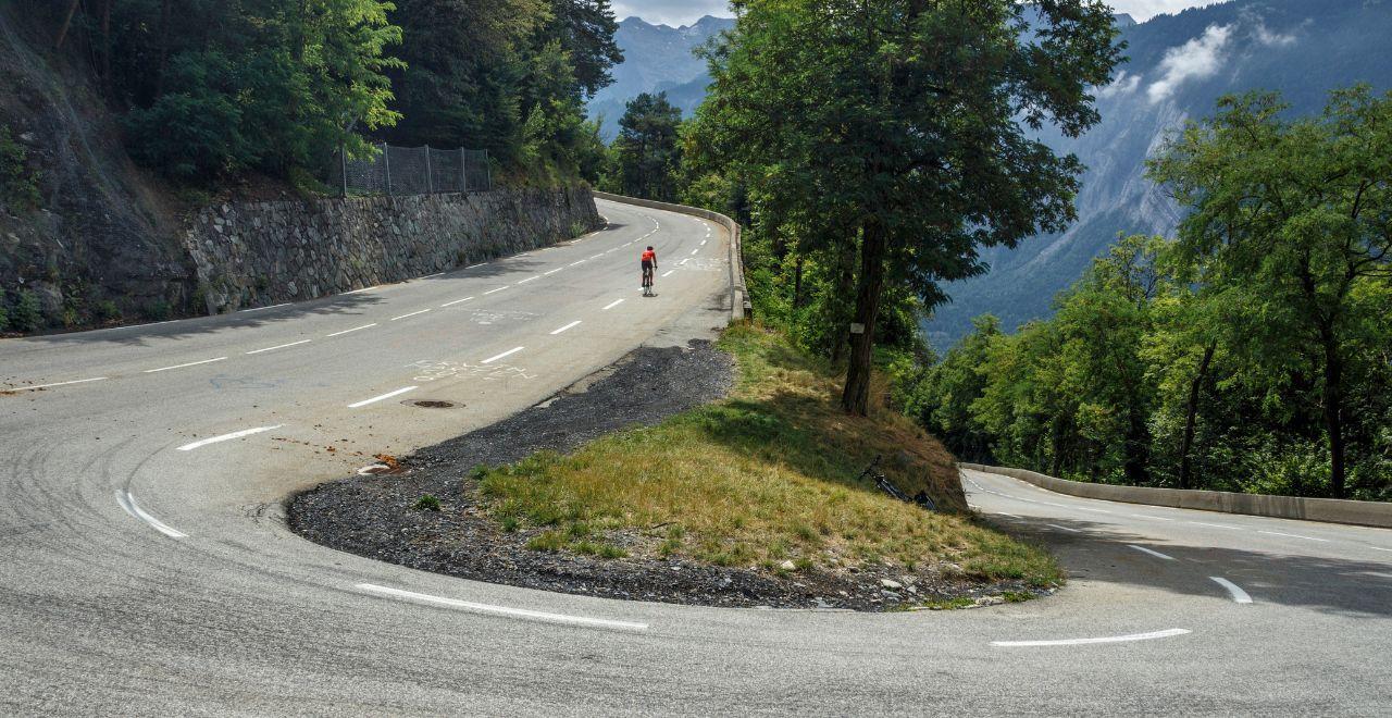 Cyclist riding uphill on a curved mountain road with scenic views.