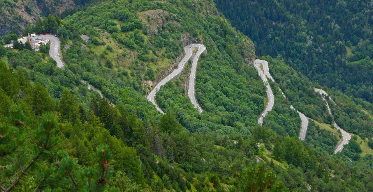 Winding mountain road through lush green forest in the Alps.
