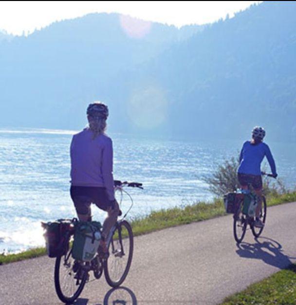 Group of cyclists enjoying a leisure ride along a riverside path with lush green mountains in the background