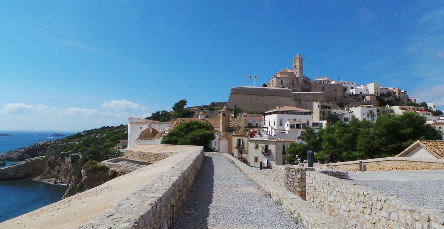 View of the old town of Ibiza with historic buildings on a hill, a stone path leading up, and the sea in the background.