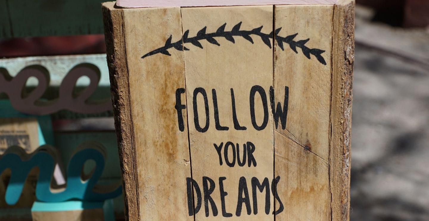 Text: Wooden sign with the phrase "Follow Your Dreams" painted on it, surrounded by blurred background elements.