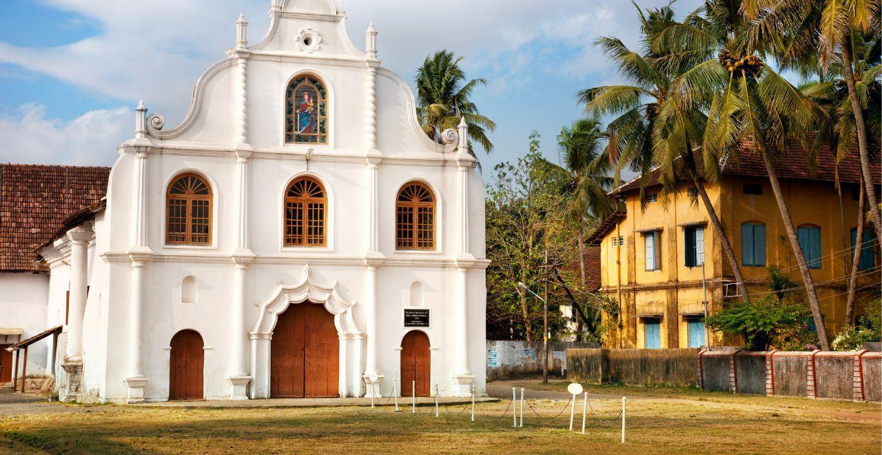Historic white church with arched windows and palm trees in Kochi, Kerala.