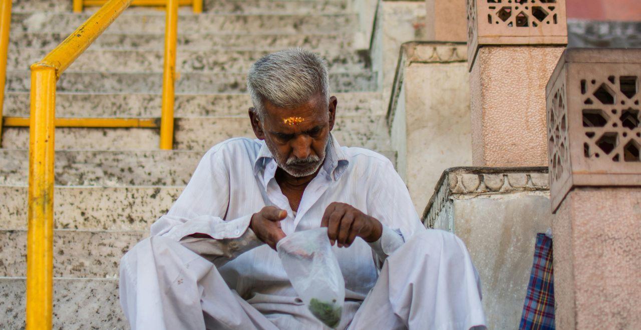 Elderly man sitting on stairs with a plastic bag in hand