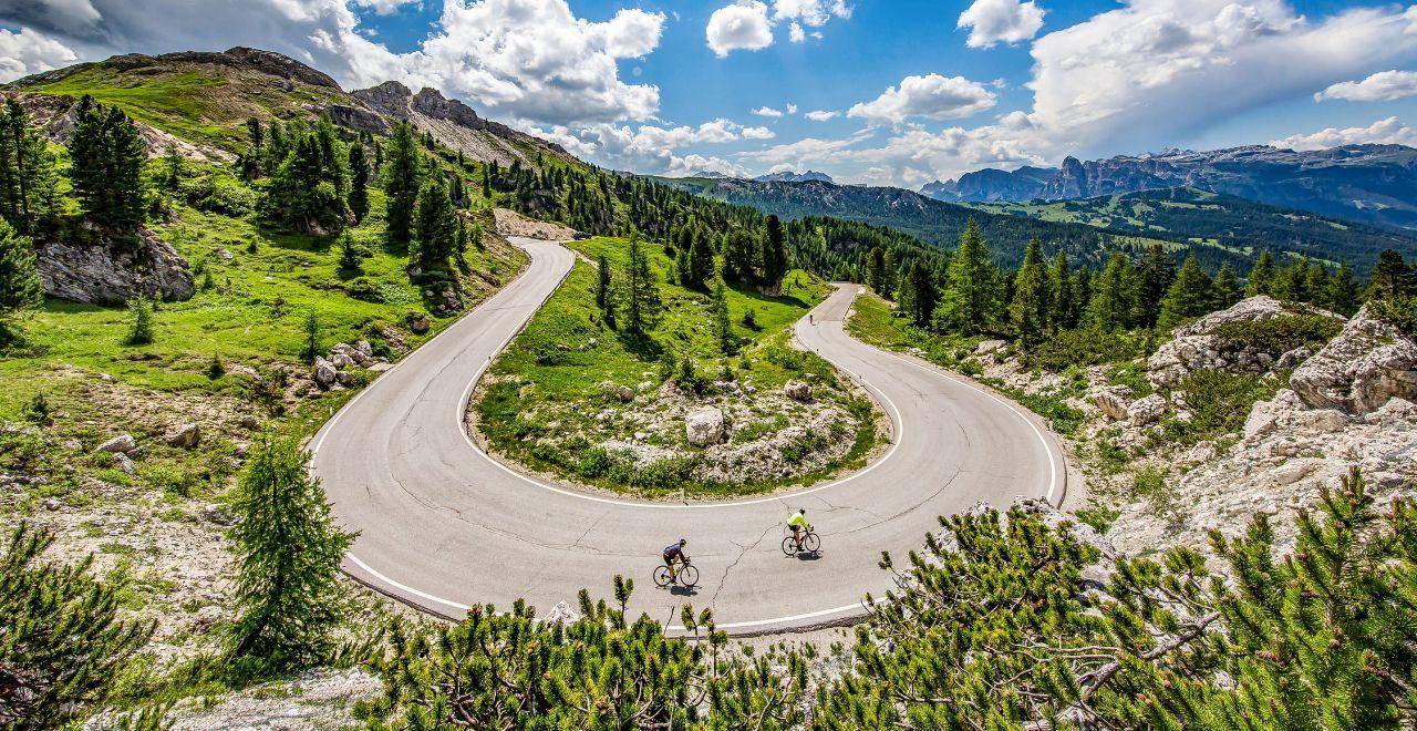 2 cyclists riding a bend in the stunning Dolomite mountains, known for its challenging climbs and breathtaking scenery.