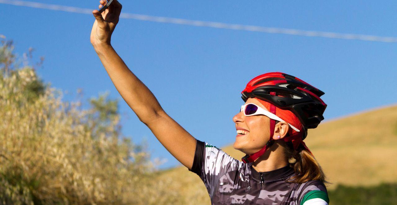 Female cyclist taking a selfie while smiling under a clear blue sky