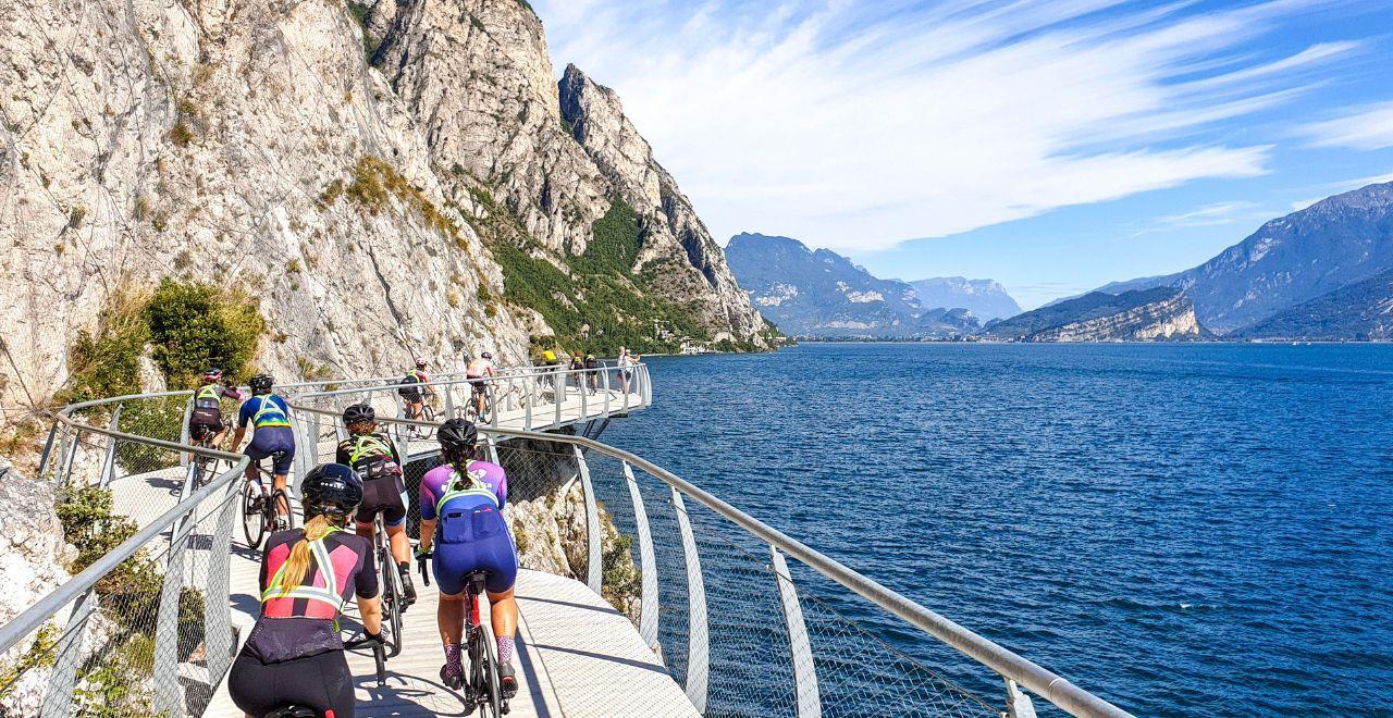 Group of cyclists riding around a suspended path over Lake Garda with mountains in the background