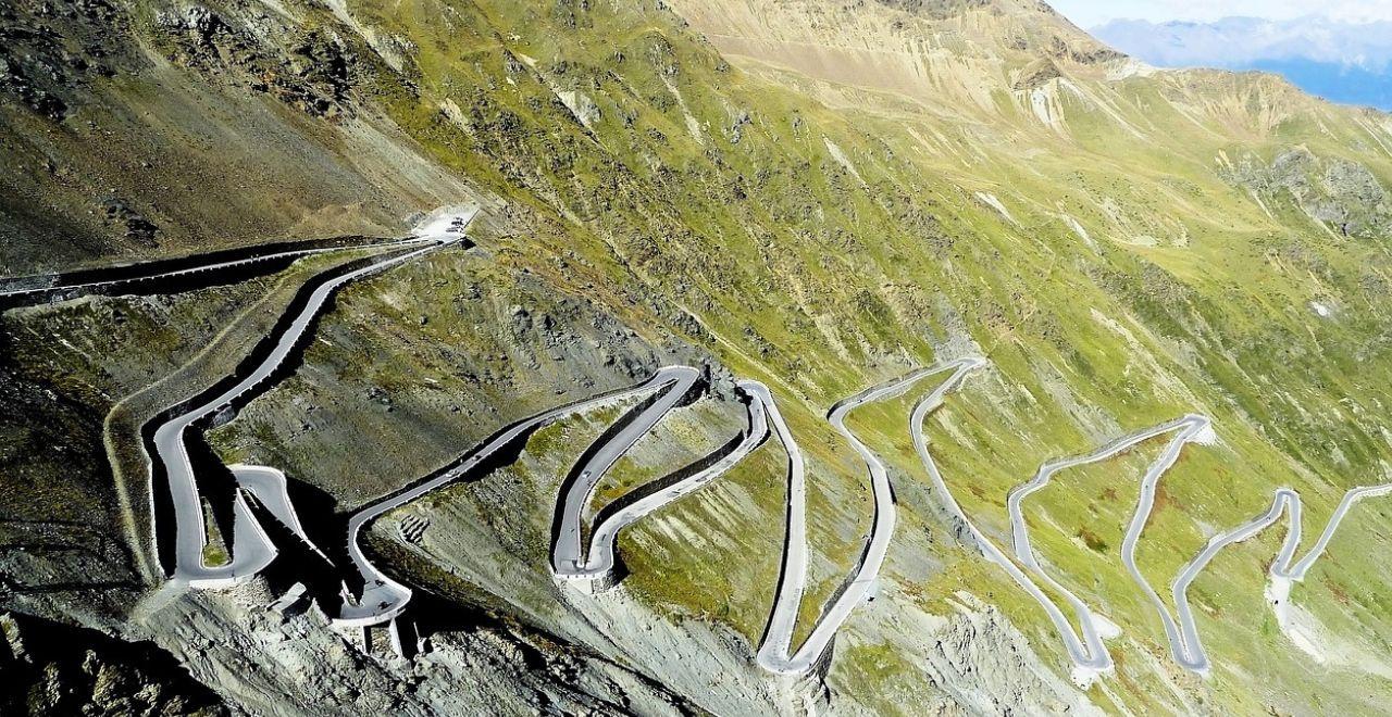 Aerial view of the Passo Stelvio mountain road with multiple hairpin turns and a valley below.