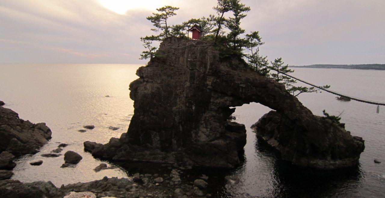 Small red shrine on a rocky cliff, ocean backdrop at sunset