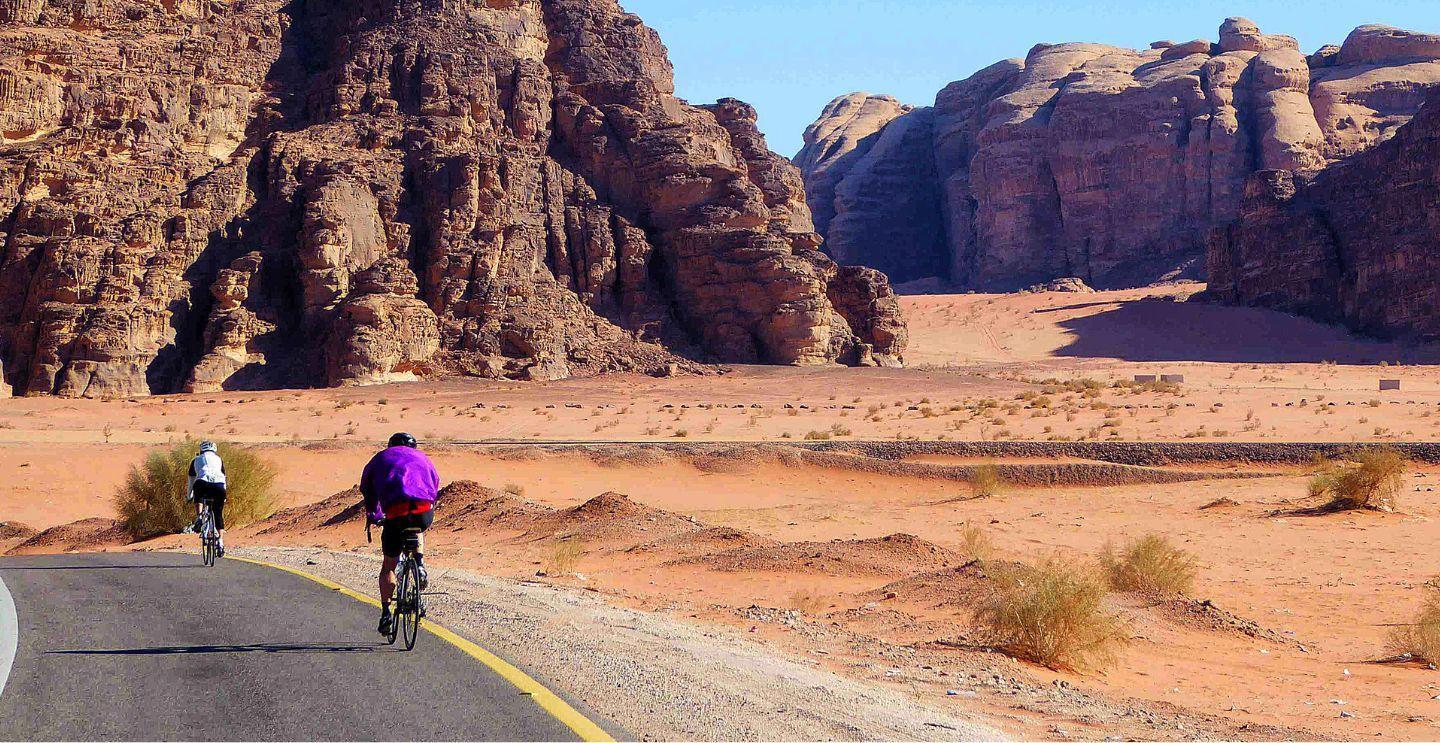 Cyclists riding through a desert road flanked by towering rock formations in Wadi Rum, Jordan.