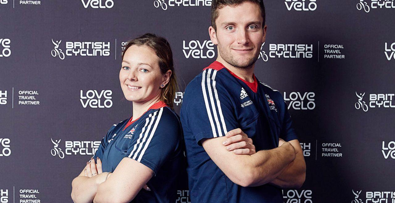 Two British cyclists posing back-to-back in front of Love Velo and British Cycling backdrop.