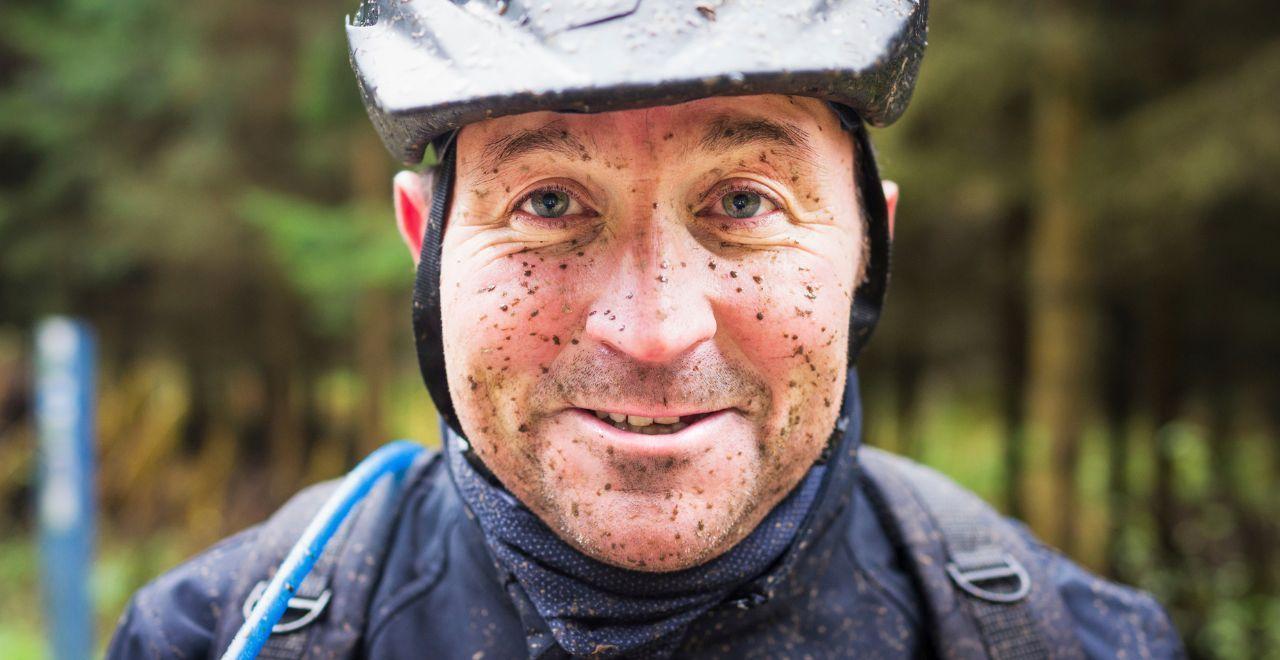 Smiling cyclist with mud on his face after a ride.